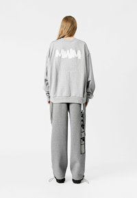 Sudadera gris de gran tamaño con un logo impreso en la parte posterior, combinada con pantalones de chándal grises que tienen detalles de diseño en blanco y negro.