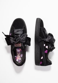 Svarta mocka sneakers med överdimensionerade svarta satinrosetter, med färgglada hjärt-mönster på sidorna och ett mönstrat inre.