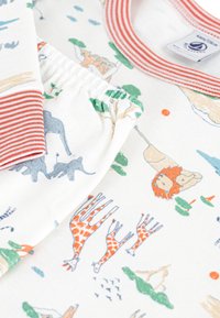 Παιδικό βαμβακερό πουκάμισο με κόκκινη λαιμόκοψη με ρίγες, που διαθέτει διάφορες ζωικές εικονογραφήσεις, συμπεριλαμβανομένων λιονταριών, καμηλοπαρδάλων και ελεφάντων, σε λευκό φόντο.