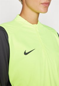 Svijetlo neon žuta zip jakna s crnim detaljima i malim crnim Nike logotipom na prsima; glatka tekstura, lagana tkanina.
