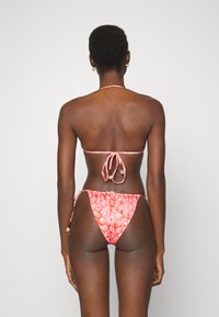 Conjunto de bikini de duas peças em coral com um padrão de conchas. Apresenta laços no pescoço e nas costas, alças laterais ajustáveis e pequenas contas decorativas.