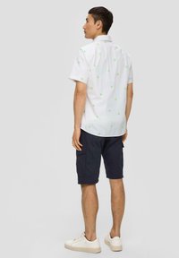 Weißes Kurzarmhemd mit grüner Palmbaumstickerei, kombiniert mit marineblauen Cargo-Shorts und weißen Sneakers, von hinten betrachtet.