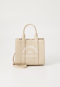 Beige texturerad handväska med dubbla topphandtag och ett avtagbart axelband. Har präglad logotyp och kontrasterande vit text på framsidan.