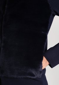 Granatowy sweter z miękką i puszystą fakturą na przodzie, gładkimi rękawami oraz zaokrąglonym dekoltem. Charakteryzuje się eleganckim designem.