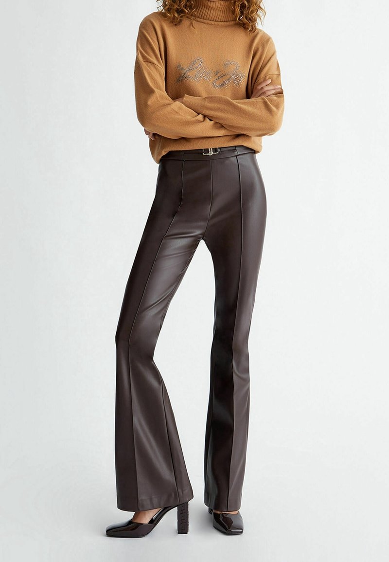 Pantalon évasé en similicuir marron avec des détails de couture verticale et une taille haute, associé à un pull à col roulé côtelé beige.