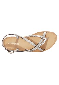 Sandali con cinturini caratterizzati da lacci intrecciati in argento, soletta in pelle marrone, suola esterna sottile e fibbia alla caviglia regolabile.