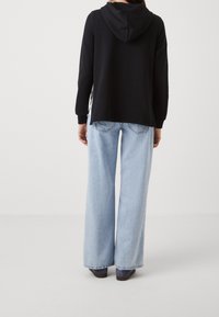 Black hooded sweatshirt with long sleeves, paired with light blue wide-leg jeans. The outfit features a relaxed fit and casual design.