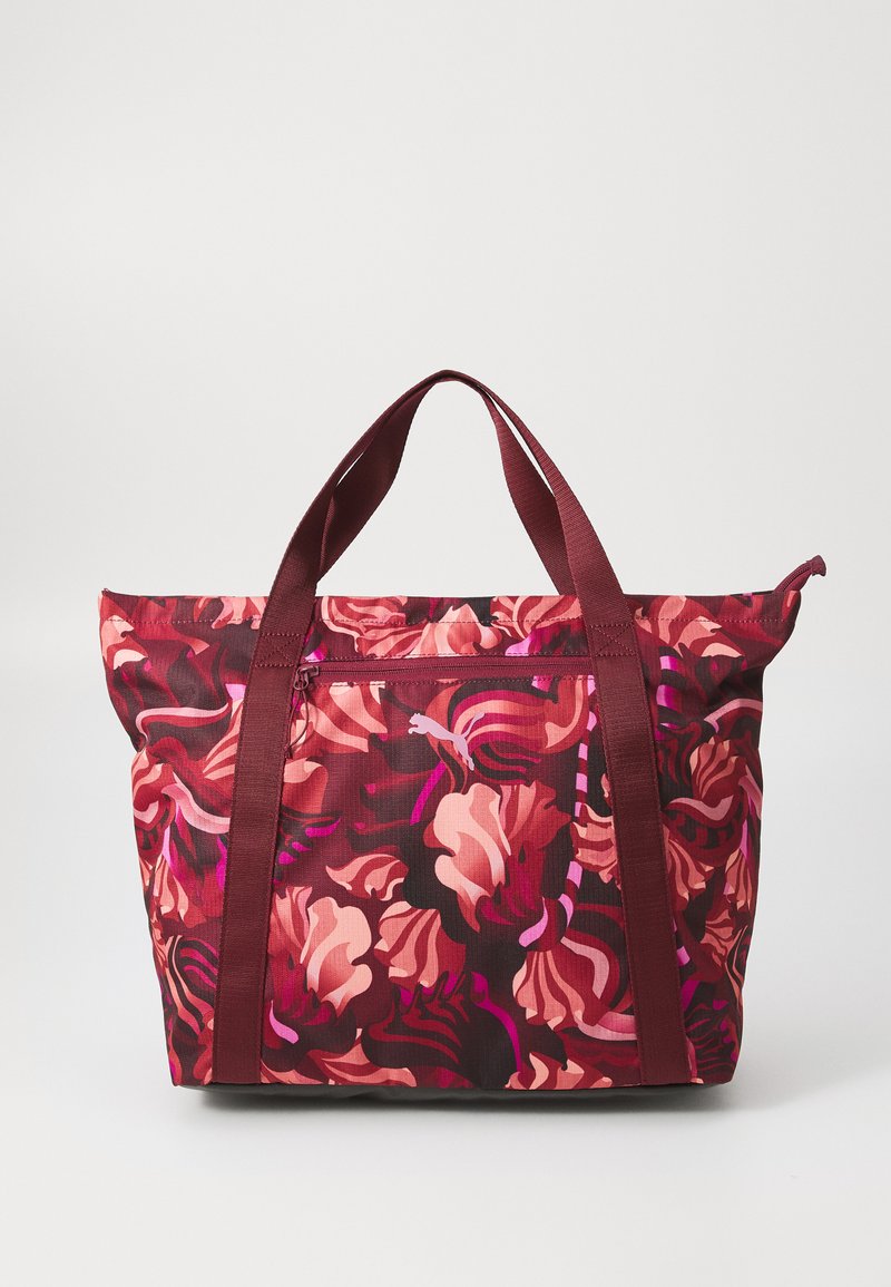 Un grand sac fourre-tout présente un motif floral vibrant dans des teintes de rose et de maroon, avec des poignées maroon robustes et une fermeture éclair.