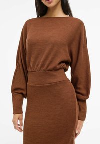 Brązowa prążkowana sukienka dzianinowa z szerokim dekoltem, luźnymi rękawami i dopasowaną talią, tworząca gładką sylwetkę.