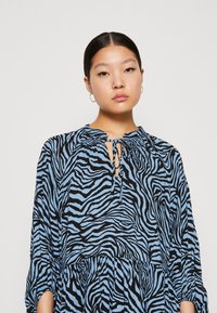 Robe à motif zèbre bleu avec un col froncé et un détail en trou de serrure. Présente des manches longues et une silhouette fluide ; fabriquée en tissu léger.