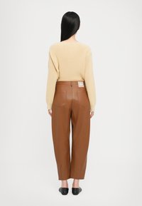Maglione a maglia beige con dettagli a coste, abbinato a pantaloni in finta pelle marrone con tasche posteriori e un'etichetta in vita. Scarpe slip-on nere.