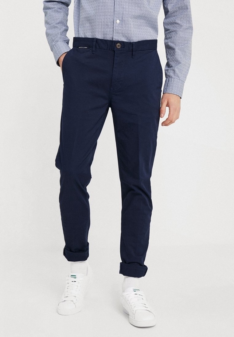 Mørkeblå chinos med lige snit, synlig stoftekstur. Kombineret med hvide sneakers, med opsmøgede bukseben og knaplukning.