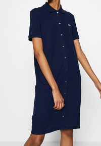 Robe polo bleu marine en coton, avec manches courtes, fermeture à boutons et une légère silhouette trapèze. Petit logo brodé sur la poitrine.