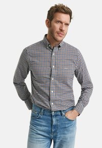 Overhemd met knoopsluiting in een marineblauw en bruin ruitpatroon, lange mouwen, spreidkraag en knoopsluiting aan de voorkant. Gecombineerd met lichtblauwe jeans.