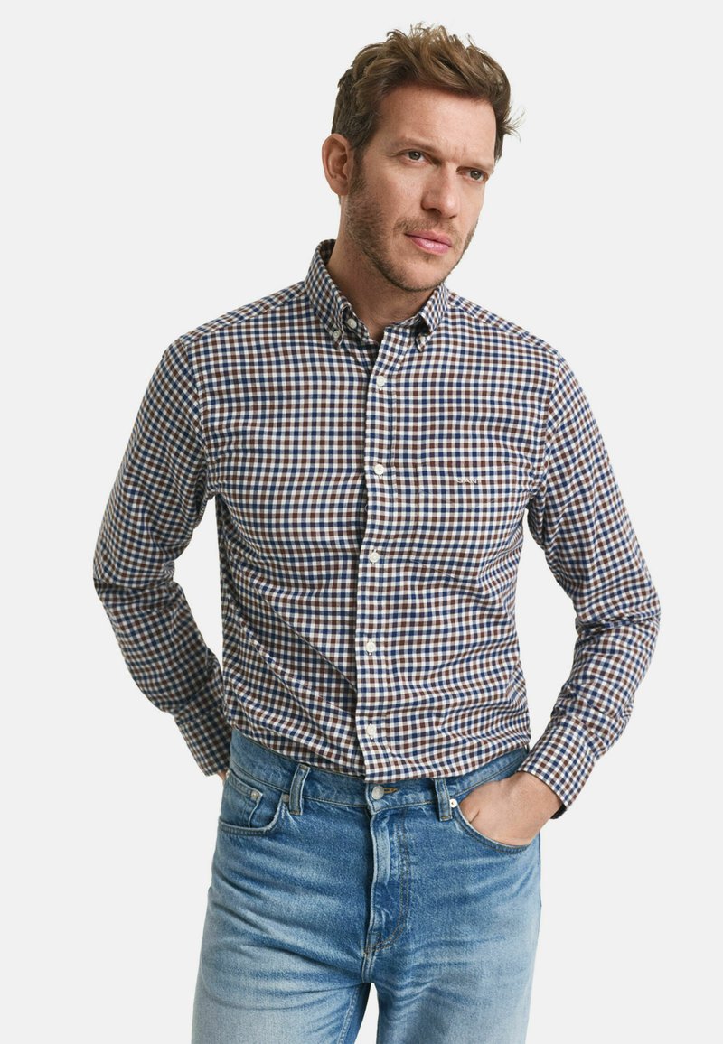 Skjorte med knapper i marineblå og brun ternet mønster, lange ærmer, bred krave og frontknaplukning. Kombineret med lyseblå jeans.
