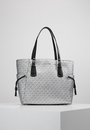 Sac cabas gris pour créateur avec poignées noires, poches latérales et motif de logo répété, posé sur une surface blanche.