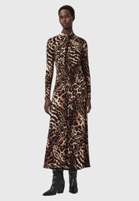 Plettet leopardkjole i strækbart stof, med krave, lange ærmer og samling ved taljen. Parret med knæhøje sorte støvler.