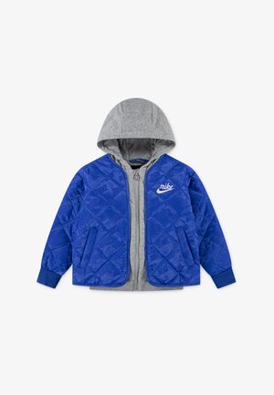 Modrá prošívaná bunda s šedou kapucí, zipovým uzávěrem, bočními kapsami a bílým logem Nike na hrudi. Měkká textura.