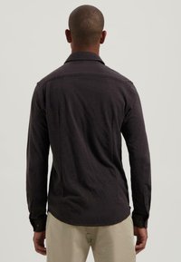 Donkergrijze langëx005fskorte shirt met een kraag, knoopmanchetten en een gladde textuur, weergegeven vanaf de achterkant tegen een neutrale achtergrond.