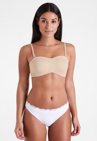 Beżowy biustonosz typu strapless z formowanymi miseczkami i regulowanymi ramiączkami, w połączeniu z białymi stringami wykończonymi koronką. Gładka tekstura, bezszwowy design.