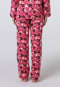 Completo pigiama floreale con fiori rosa, bianchi e neri su uno sfondo rosa chiaro. Pantaloni morbidi con gamba dritta e polsini a costine.