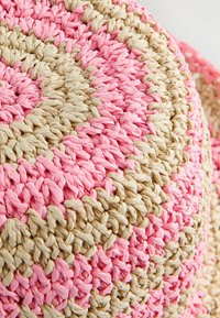Runder, gewebter Kissenbezug aus rosa und beigen Fasern, mit einer strukturierten Oberfläche und einem Spiraldesign, das durch abwechselnde Farben entsteht.