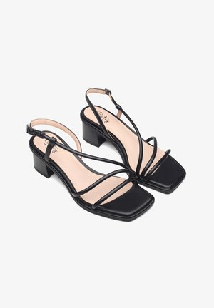 Black strappy sandals with a square toe, made of smooth leather, featuring a low block heel and an adjustable ankle strap.