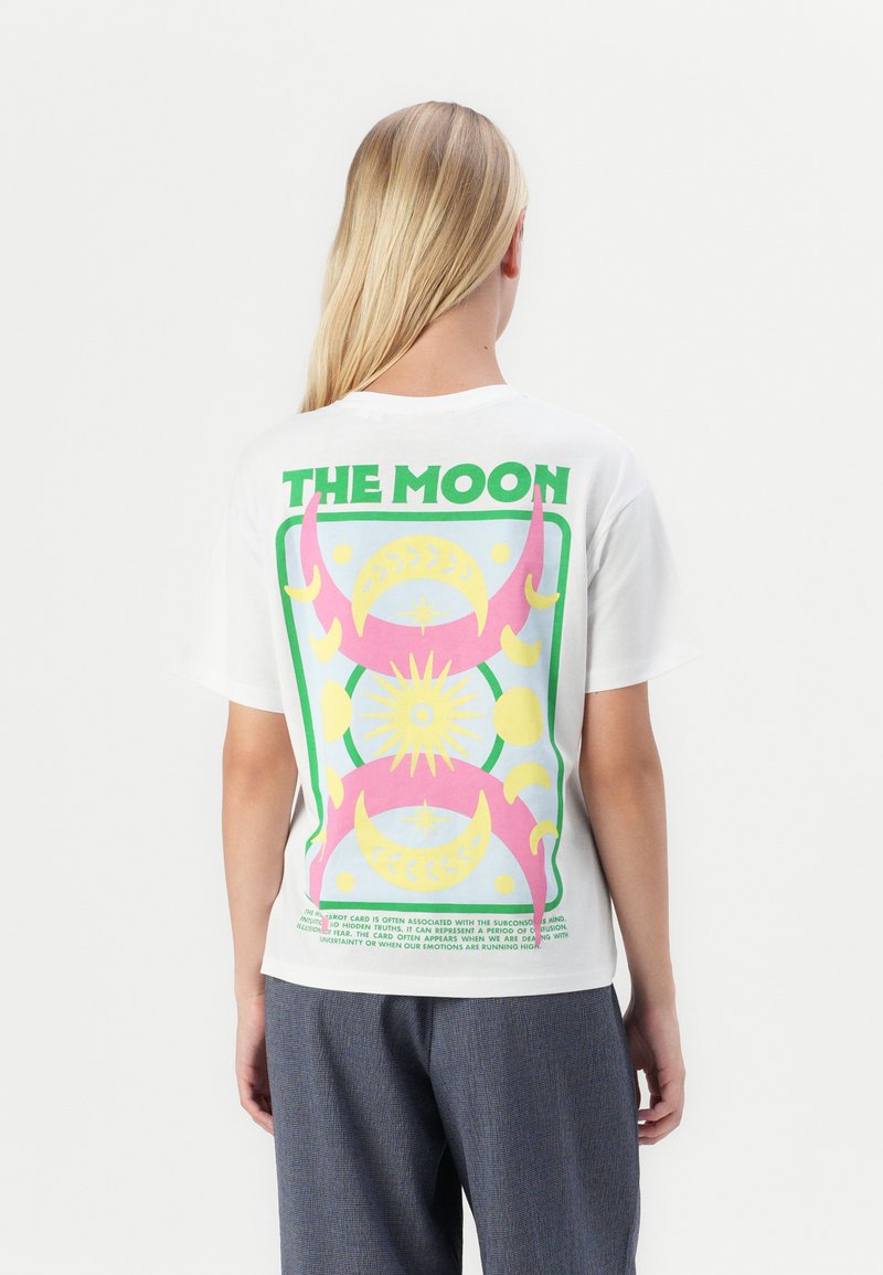 Hvit bomulls-T-skjorte med et fargerikt grafisk design på baksiden med teksten "THE MOON" i grønne, rosa og gule elementer og former.