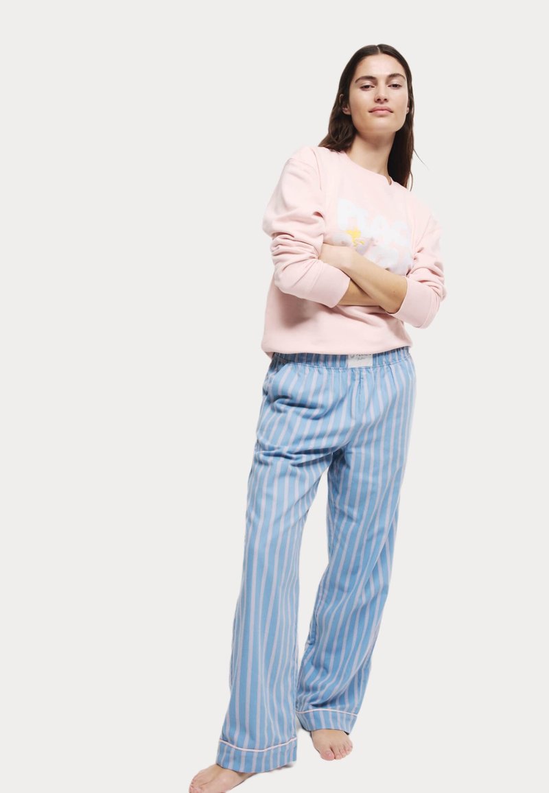 Rosa sweatshirt med vit grafisk design, parat med ljusblå randiga pyjamasbyxor. Bekväm passform, mjukt tyg och avslappnad stil.