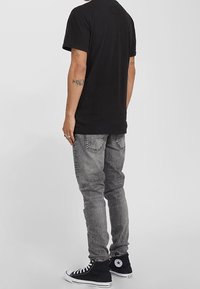 Svart bomullströja med en enkel design, i kombination med grå denimjeans och svarta högskaftade sneakers med en vit logotyp och snören.