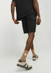 Chemise surdimensionnée noire texturée, shorts assortis, baskets beiges avec accents foncés, et chaussettes marron avec un design graphique.