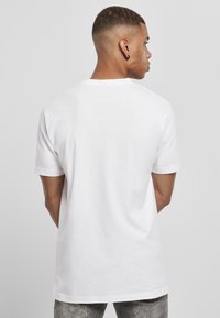 Kortærmet hvid T-shirt med rund hals, lavet af bomuld, med en glat tekstur og en afslappet pasform, vist fra ryggen.