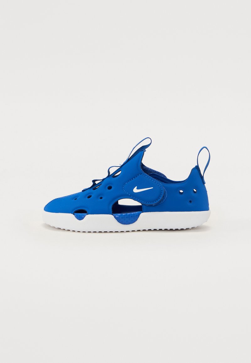 Blauer Sportschuh aus glattem Gummi mit Belüftungsöffnungen, weißer Sohle, verstellbarem Schnürsenkel und Nike-Logo an der Seite.