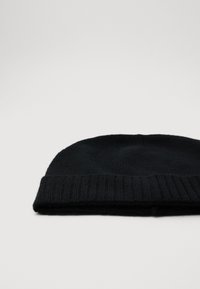 Gorro de punto negro con puño acanalado doblado, colocado sobre un fondo gris claro.