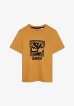 T-shirt jaune moutarde en coton, avec un graphique d'arbre noir à l'intérieur d'un carré et le mot "Timberland" en bas. Col rond.
