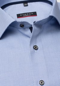 Chemise à manches longues bleu clair à motifs, avec une texture tissée, des boutons noirs et un col à coupe moderne. Étiquette Eterna visible à l'intérieur du col.