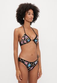 Μαύρο σετ μπικίνι με τριγωνικό τοπ και σλιπ με ισχνούς ιμάντες, διακοσμημένο με πολύχρωμα κέλυφη και αστέρια της θάλασσας. Ρυθμιζόμενοι ιμάντες δέσιμο.
