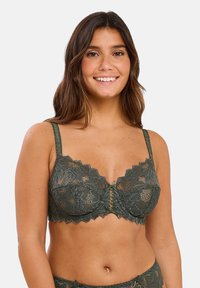 Reggiseno verde in pizzo con bordi scallop, dettaglio centrale con lacci e spalline sottili e regolabili. Motivo floreale intricato su tutto il tessuto.