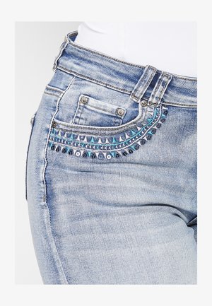 Heledad sinine teksapüksid, mille esikoti kaunistavad sinised ja hõbedased dekoratiivsed detailid. Omab klassikalist viie tasku disaini.