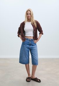 Culotte in denim azzurro chiaro, con vita alta e orlo all'altezza del ginocchio. Abbinato a un crop top bianco e a un cardigan marrone scuro.