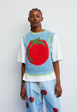 Strikkevest med et rødt tomatmotiv på en lyseblå baggrund med grønne accenter. Sat sammen med en hvid skjorte og stribede bukser.