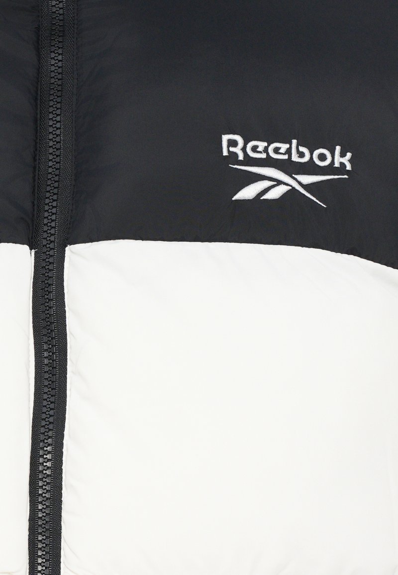 Czarna i biała kurtka puchowa z zapięciem na zamek, z wyraźnie haftowanym logo Reebok na piersi oraz gładkim, teksturowanym wykończeniem.