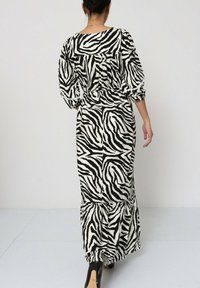 Robe maxi avec imprimé zèbre noir et blanc, manches bouffantes, ourlet à volants et taille cintrée ; le tissu semble léger et texturé.