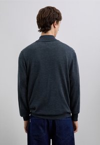 Dunkelgrauer Strickpullover mit Kragen und langen Ärmeln. Glatte Textur, lockere Passform, getragen mit blauen Jeanshosen. Einfaches Design, ohne Muster.