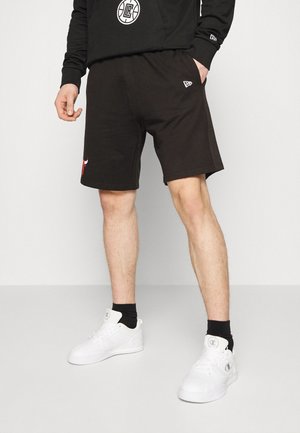 Shorts neri in cotone con vita elastica, caratterizzati da un logo di toro rosso e un piccolo emblema bianco. Indossati con sneakers bianche e calzini neri.