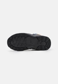 Czarna podeszwa buta Nike z głębokim bieżnikiem i teksturowanym uchwytem, leżąca na płasko na białym tle, ukazująca szczegółowy wzór bieżnika i logo.