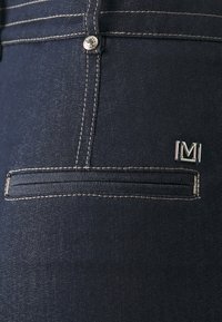 Jeans in denim scuro con chiusura a bottone argentato, cuciture a contrasto e un piccolo logo metallico sul taschino posteriore con un design inset.