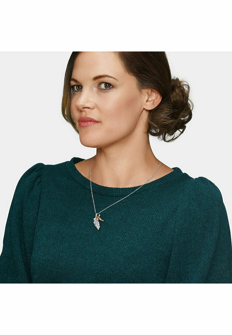 Sølv halskæde med et bladformet vedhæng, båret med en tekstureret grøn sweater. Vedhænget har en detalje i guld.