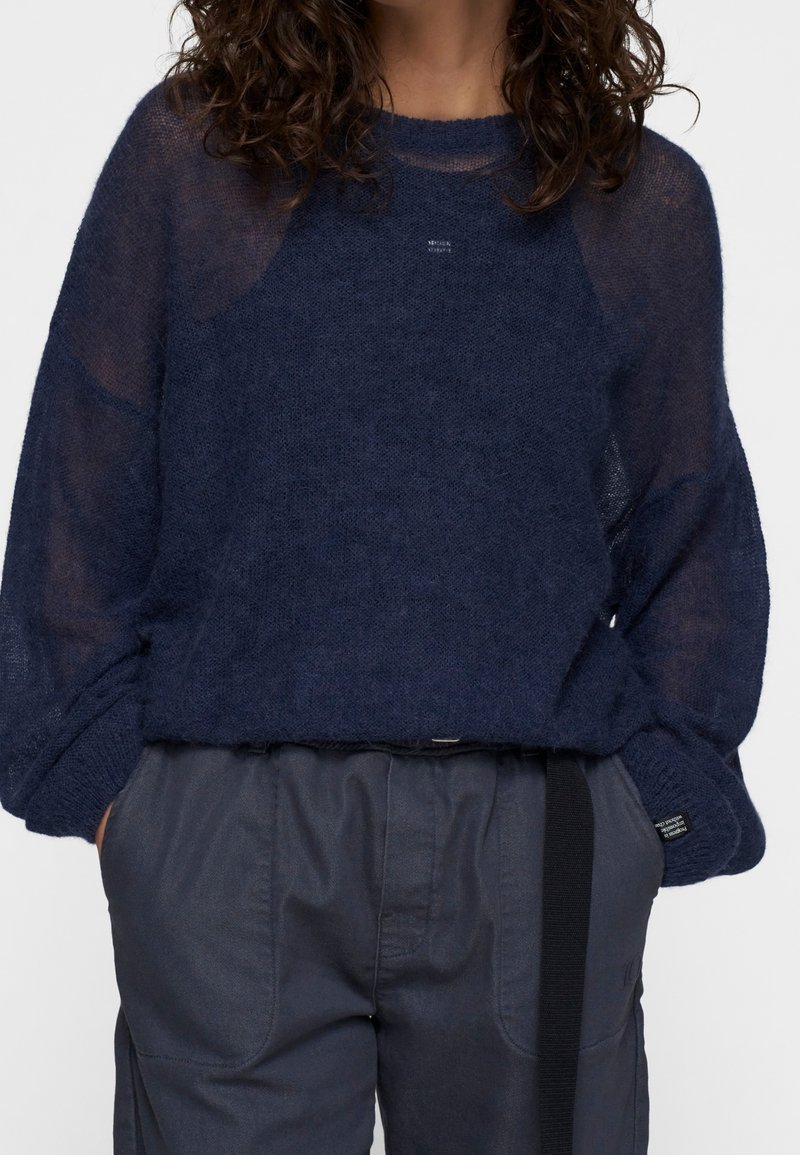 Granatowy sweter o luźnej, przejrzystej strukturze z rękawami typu raglan. W zestawie z ciemnoszarymi spodniami z kontrastującym, czarnym pasem w talii.