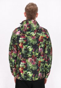 Jachetă cu glugă, având un model vibrant, multicolor de frunze tropicale pe un fundal negru. Confecționată dintr-un material ușor, texturat.